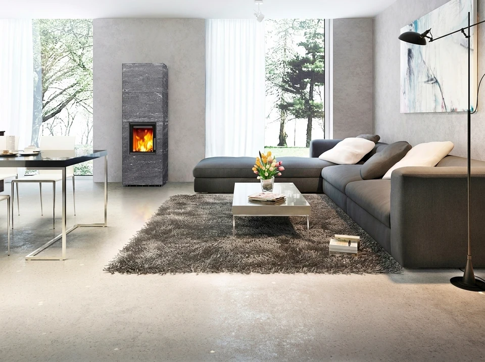 Pièce vide avec poêle à bois contemporain autoportant, habillage en pierre ollaire (stéatite) grise veinée de blanc, insert vitré à cadre noir avec chambre de combustion visible dorée